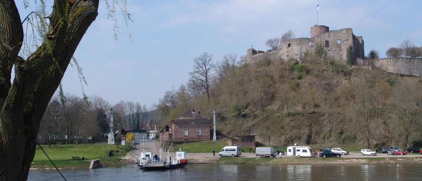 Blick auf die historische Burg Polle mit der Weser im Vordergrund, eine Fähre kreuzt den Fluss.