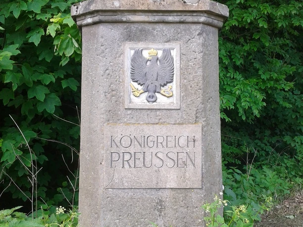 Hoheitsstein in Harzberg Steinerner Hoheitsstein in Harzberg mit preußischem Adler, umgeben von dichter Vegetation.