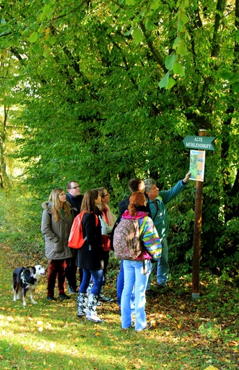 Mühlendrift 1 Eine Gruppe von Menschen mit einem Hund liest ein Wegweiserschild im bewaldeten Gebiet Alte Mühlendrift.