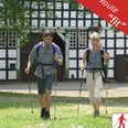 Nordic Walking - fit Zwei Personen genießen eine Nordic Walking Tour vor einem traditionellen Fachwerkhaus.