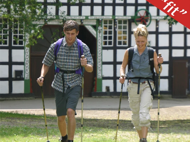 Nordic Walking - fit Zwei Personen genießen eine Nordic Walking Tour vor einem traditionellen Fachwerkhaus.