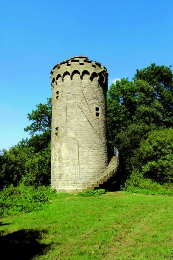 Auf unserer Wanderung kommen wir am Holsterturm vorbei. Ein historischer Steinturm mit Wendeltreppe steht von Bäumen umgeben im Grünen unter klarem Himmel.