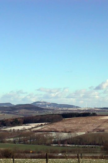 Dieser herrliche Ausblick erwartet uns auf dem Holsterbergrundweg. Weite Landschaft mit sanften Hügeln unter blauem Himmel, vereinzelt Bäume und Felder im Winterkleid.