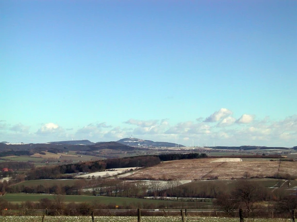 Dieser herrliche Ausblick erwartet uns auf dem Holsterbergrundweg. Weite Landschaft mit sanften Hügeln unter blauem Himmel, vereinzelt Bäume und Felder im Winterkleid.