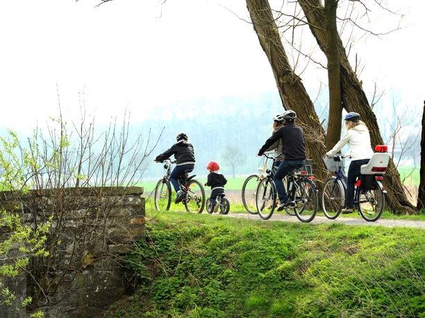 Radler am Boker Kanal Radfahrer, darunter ein Kind, fahren entlang eines grünen Weges am Ufer des Boker Kanals entlang.