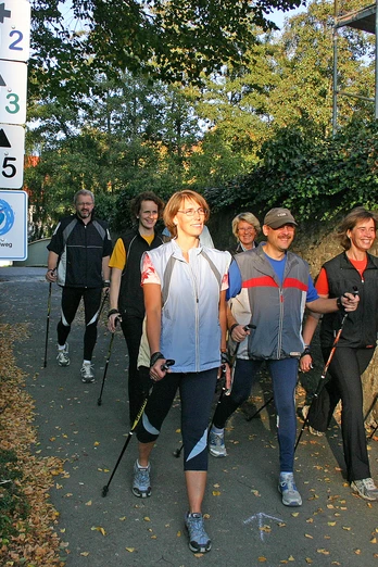 Eine Gruppe von Menschen beim Nordic Walking auf einem herbstlichen Waldweg mit Wegweisern.