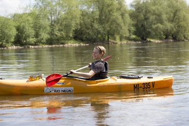 Mit dem Kanu auf der Weser Person in einem orangefarbenen Kanu paddelt auf einem ruhigen Fluss, umgeben von grüner Natur.