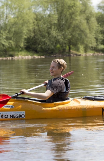 Mit dem Kanu auf der Weser Person in einem orangefarbenen Kanu paddelt auf einem ruhigen Fluss, umgeben von grüner Natur.