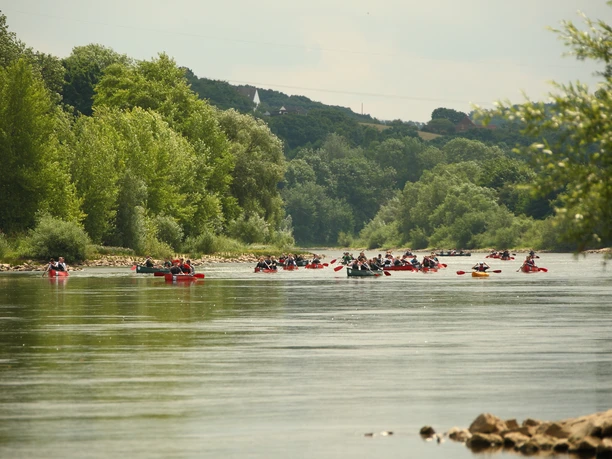 Mit dem Kanu auf der Weser Kanutour auf der Weser: Paddler gleiten gemächlich über den breiten Fluss, umgeben von grünen Uferbäumen.