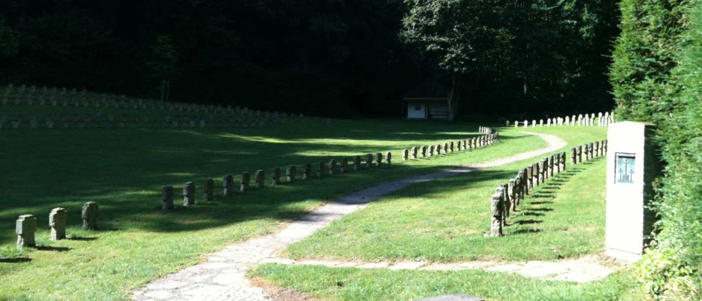 Kriegsgräberstätte Altenböddeken Eine friedvolle Kriegsgräberstätte mit gepflegtem Rasen, umgeben von ruhigem Wald, lädt zum Gedenken ein.
