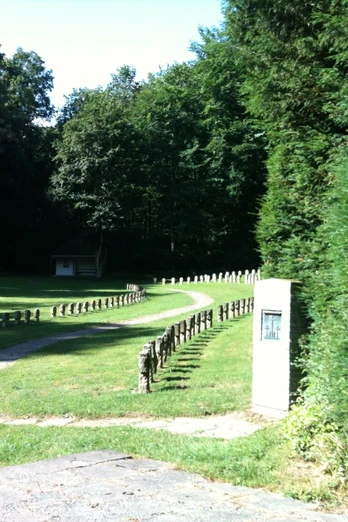 Kriegsgräberstätte Altenböddeken Eine friedvolle Kriegsgräberstätte mit gepflegtem Rasen, umgeben von ruhigem Wald, lädt zum Gedenken ein.