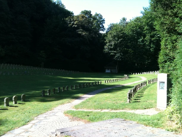 Kriegsgräberstätte Altenböddeken Eine friedvolle Kriegsgräberstätte mit gepflegtem Rasen, umgeben von ruhigem Wald, lädt zum Gedenken ein.