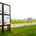 Infotafel und Wegweiser im Römerlager Anreppen, umgeben von einer weiten Wiesenlandschaft.