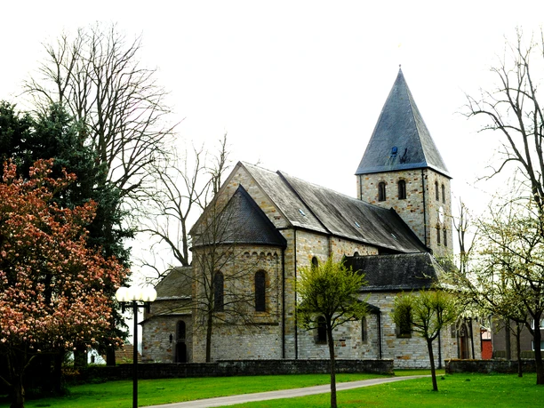 Kirche in Boke Historische Steinkirche mit Turm umgeben von blühenden Bäumen vor einem klaren Frühlingshimmel.