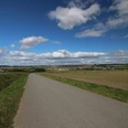 Blick auf Dalhausen (rechts), Borgholz (Mitte) und Natzungen (links). Weite Felder und Wiesen erstrecken sich vor einer ländlichen Straße, unter einem blauen Himmel mit Wolken.
