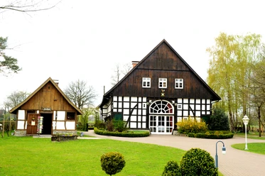 Das Gastliche Dorf Ein Fachwerkgebäude mit weißen Wänden und dunklen Balken steht in gepflegter Gartenanlage.