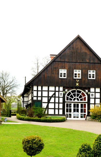 Das Gastliche Dorf Ein Fachwerkgebäude mit weißen Wänden und dunklen Balken steht in gepflegter Gartenanlage.