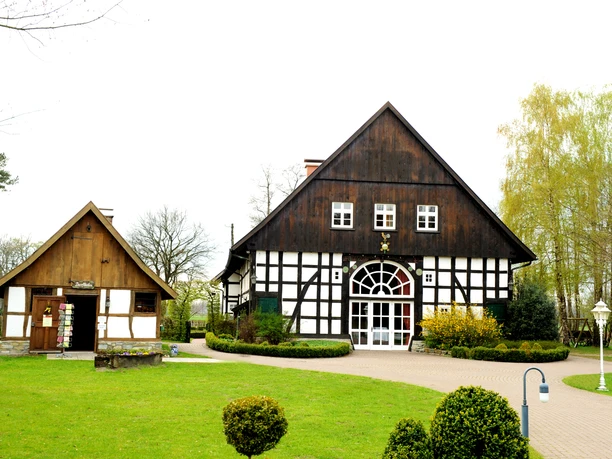 Das Gastliche Dorf Ein Fachwerkgebäude mit weißen Wänden und dunklen Balken steht in gepflegter Gartenanlage.