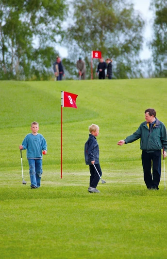 Kinder und Erwachsener beim Swin-Golf auf grüner Anlage mit rotem Fähnchen der Bahn 9.