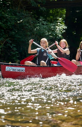 Kanutour Bega und Werre Drei Personen paddeln in einem roten Kanu auf einem flachen, klaren Fluss unter sonnigem Himmel.