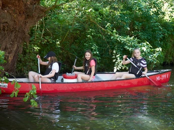 Kanutour Bega und Werre Drei junge Menschen paddeln fröhlich in einem roten Kanu auf einem grünen Fluss umgeben von Bäumen.