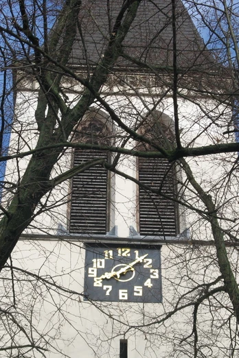 St. Antonius Kirche Der Turm der St. Antonius Kirche mit einer großen Uhr, umgeben von kahlen Bäumen vor blauem Himmel.
