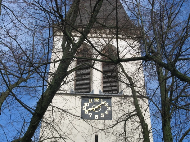 St. Antonius Kirche Der Turm der St. Antonius Kirche mit einer großen Uhr, umgeben von kahlen Bäumen vor blauem Himmel.