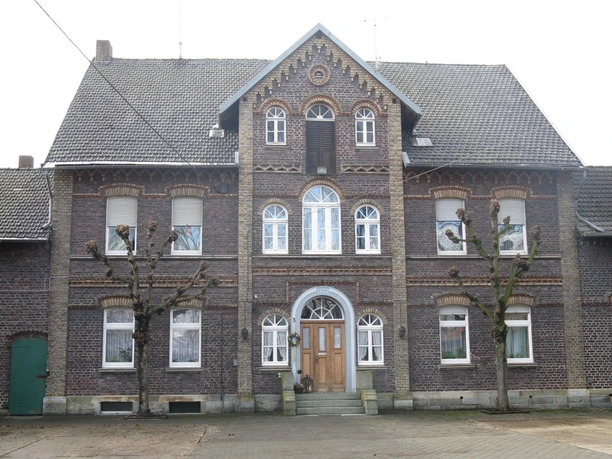 Hof Benteler Historisches Gebäude aus Backstein mit symmetrischem Design, großen Fenstern und zwei beschnittenen Bäumen davor.