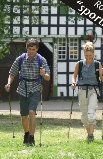 Nordic Walking - sportlich Zwei Personen nordic walken fröhlich vor einem historischen Fachwerkgebäude bei sonnigem Wetter.