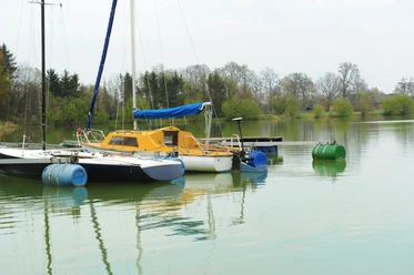 See am See Hof Franke Segelboote am ruhigen See mit grüner Umgebung und Bäumen im Hintergrund, teils bewölkter Himmel.
