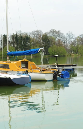 See am See Hof Franke Segelboote am ruhigen See mit grüner Umgebung und Bäumen im Hintergrund, teils bewölkter Himmel.