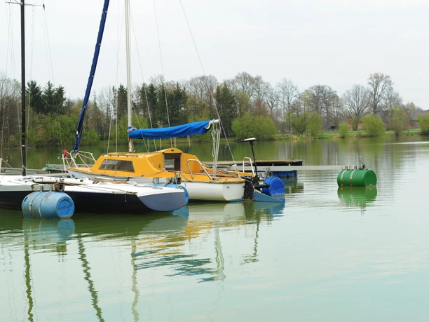 See am See Hof Franke Segelboote am ruhigen See mit grüner Umgebung und Bäumen im Hintergrund, teils bewölkter Himmel.