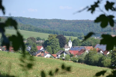 Ausblick auf das Amseldorf Merlsheim Blick über eine grüne Wiese auf die malerische Ortschaft Merlsheim, umgeben von sanften Hügeln.