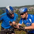 image Zwei Radfahrer in sportlicher Kleidung prüfen mithilfe eines GPS-Geräts ihren Weg vor einer Stadt.
