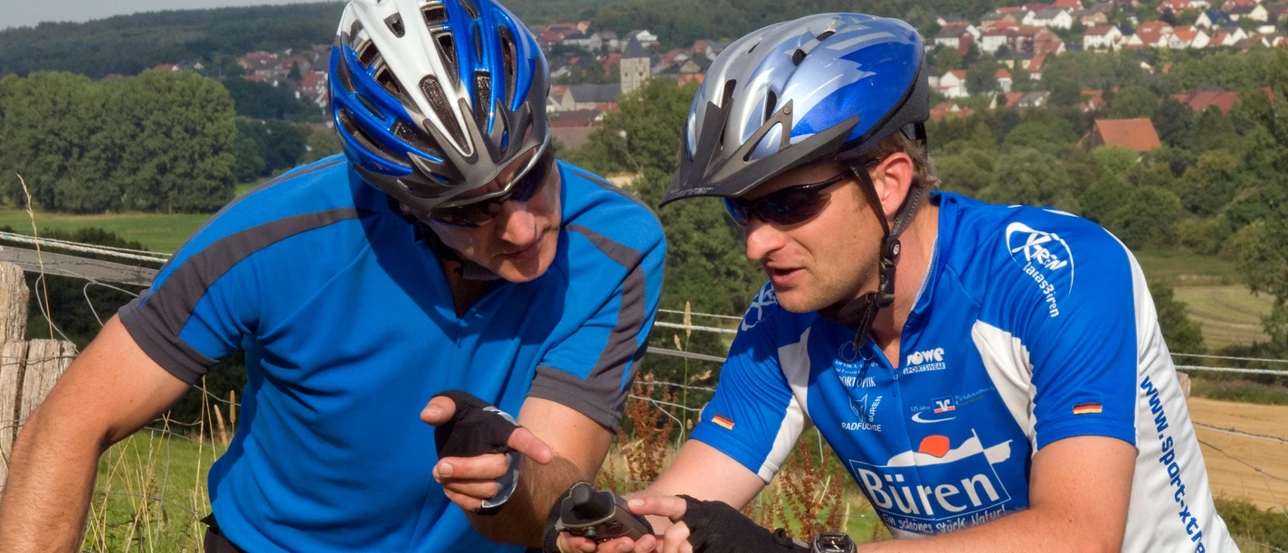 image Zwei Radfahrer in sportlicher Kleidung prüfen mithilfe eines GPS-Geräts ihren Weg vor einer Stadt.