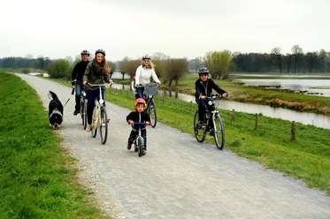 Radler am Steinhorster Becken Radfahrer mit Hund und Kind auf einem Schotterweg entlang eines ruhigen Gewässers in ländlicher Umgebung.