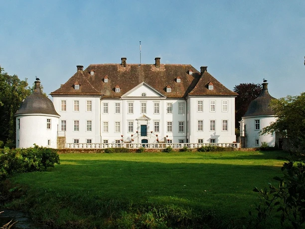 Schloss Vinsebeck, ein barockes Wasserschloss, umgeben von einer gepflegten Rasenfläche und zwei Türmen.