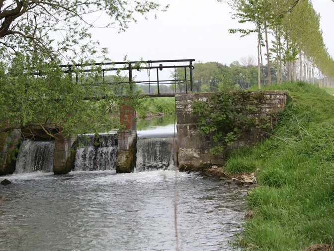 Schleuse am Boker Kanal Steinernes Bauwerk mit Schleuse über ruhigem Fluss, von Bäumen gesäumte Allee im Hintergrund.