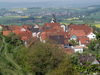Blick vom Burgberg auf das Stadtwasser Blick auf eine kleine Stadt mit roten Dächern und einer Kirche, umgeben von grünen Feldern und Hügeln.