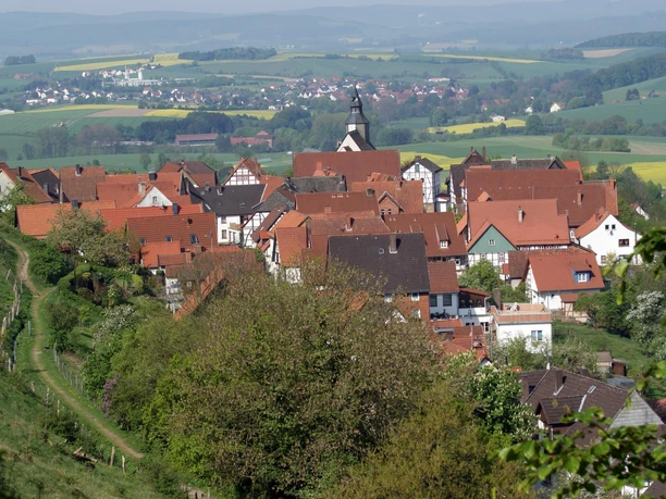 Blick vom Burgberg auf das Stadtwasser Blick auf eine kleine Stadt mit roten Dächern und einer Kirche, umgeben von grünen Feldern und Hügeln.
