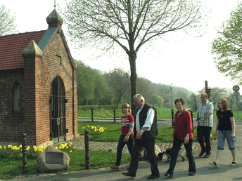 Wandergruppe an der Markuskapelle Eine Wandergruppe passiert die historische Markuskapelle, umgeben von blühenden Frühlingsblumen.