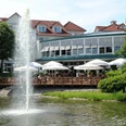 Gerry Weber Sportpark Hotel - Terrasse Terrasse des Gerry Weber Sportpark Hotels mit Sonnenschirmen am Teich und Wasserfontäne im Vordergrund.