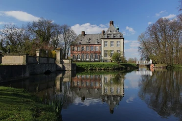 image Historisches Herrenhaus inmitten einer ruhigen Landschaft, reflektierend in einem stillen Gewässer.