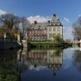 image Historisches Herrenhaus inmitten einer ruhigen Landschaft, reflektierend in einem stillen Gewässer.