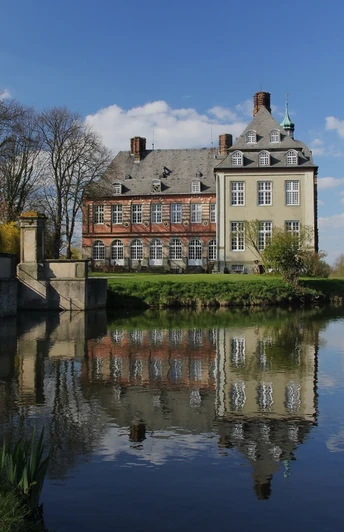 image Historisches Herrenhaus inmitten einer ruhigen Landschaft, reflektierend in einem stillen Gewässer.
