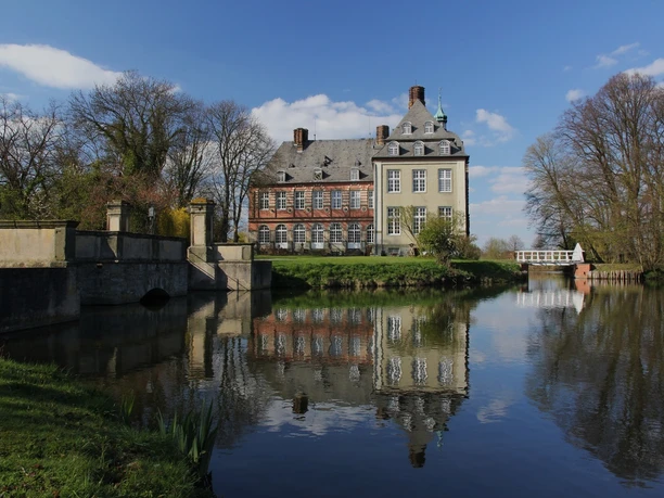 image Historisches Herrenhaus inmitten einer ruhigen Landschaft, reflektierend in einem stillen Gewässer.