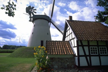 Wegholmer Mühle Historische Windmühle und Fachwerkhaus in ländlicher Umgebung bei sonnigem Wetter mit Wolken am Himmel.