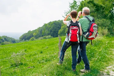 Herrlicher Ausblick vom Jakobsberg in Steinhagen Ein Paar mit Wanderrucksäcken blickt von einer grünen Wiese aus mit Ferngläsern in die Ferne.