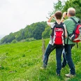 Herrlicher Ausblick vom Jakobsberg in Steinhagen Ein Paar mit Wanderrucksäcken blickt von einer grünen Wiese aus mit Ferngläsern in die Ferne.