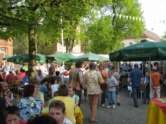 Steinheim, Festszene Menschen genießen bei sonnigem Wetter ein Straßenfest mit Ständen und grünen Schirmen im Freien.